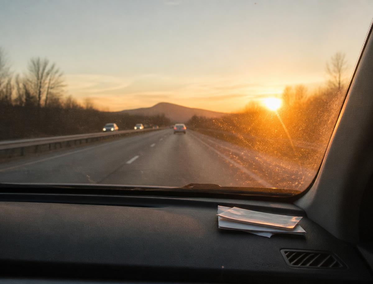 Open highway at sunset seen through a windshield with toll receipts on the dashboard